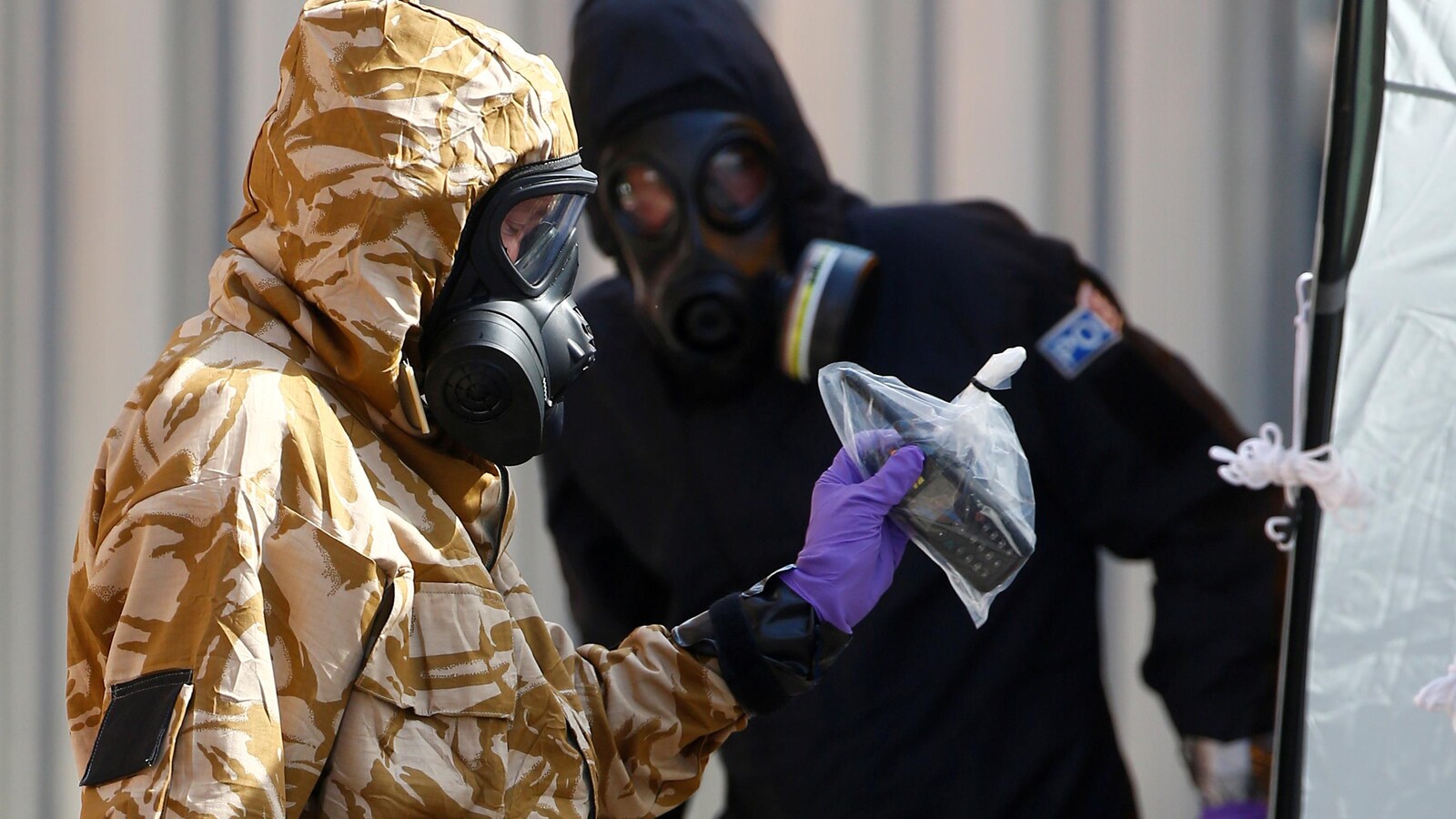 Deux hommes en habit de protection, un d'entre eux tient un téléphone dans un sac de plastique.