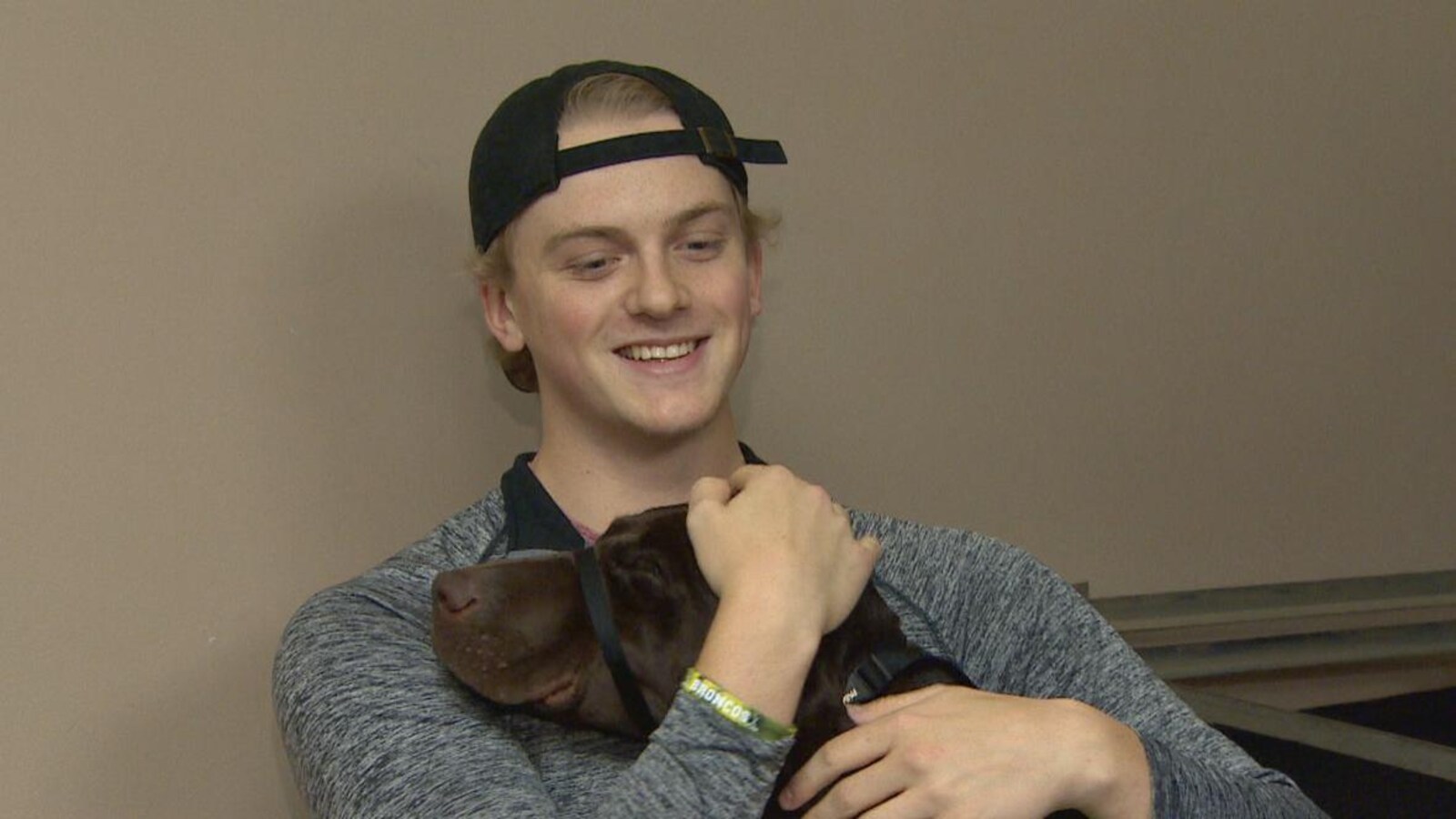 Un jeune homme portant une casquette à l'envers serre un chien dans ses bras.