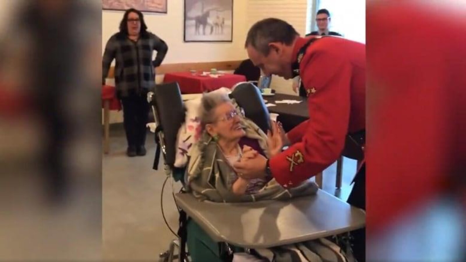 L'agent de la GRC en uniforme tient la main de Elsie Shepherd pour danser, pendant qu'elle, toute souriante, est assise sur son fauteuil roulant.