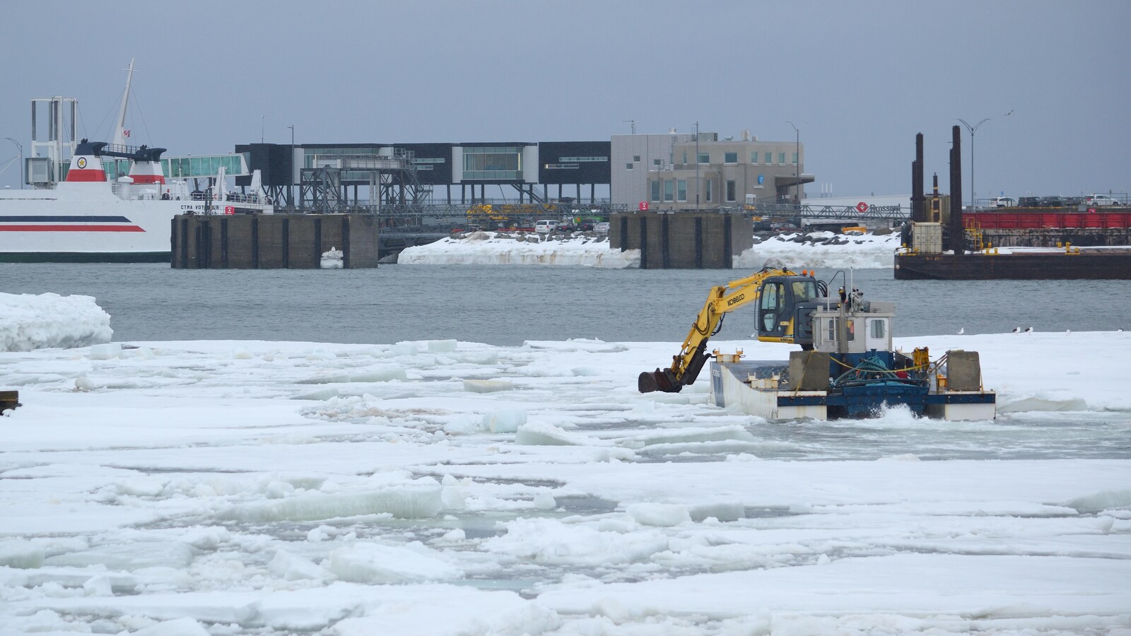 Une pelle mécanique sur une embarcation flottante casse de la glace au port de Matane.