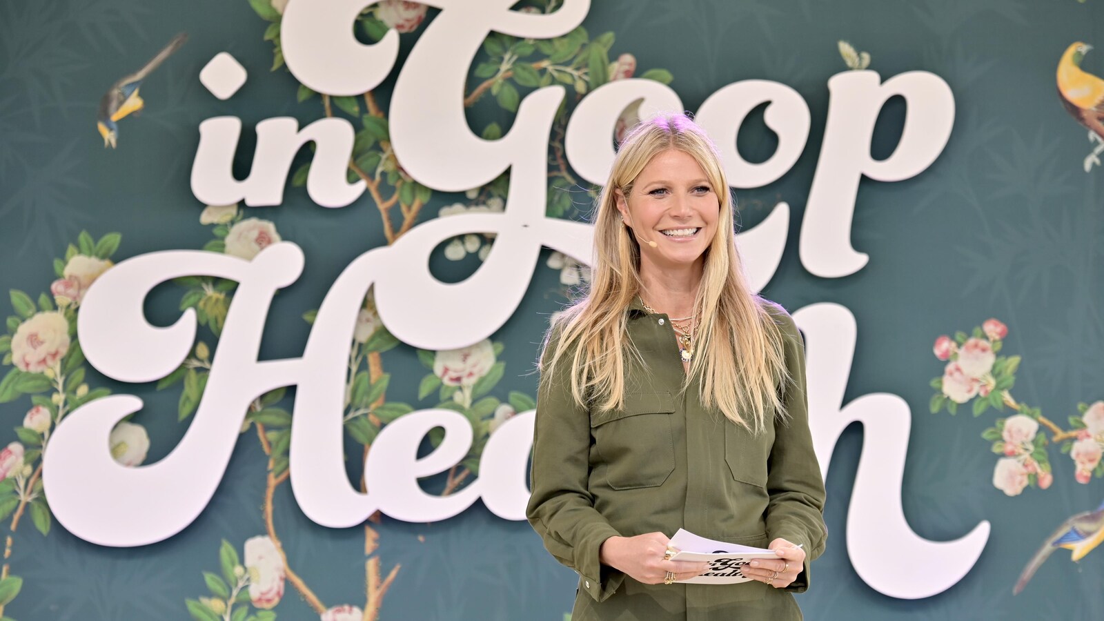Gwyneth Platrow sur une scène. Elle tient des cartons dans ses mains. Derrière elle apparaît en grosses lettres le nom de l'événement.