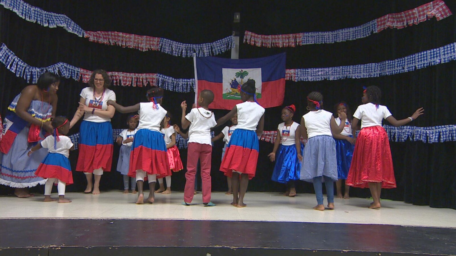 Un groupe de jeune en train de danser sur scène. Ils portent les couleur du drapeau haïtien.