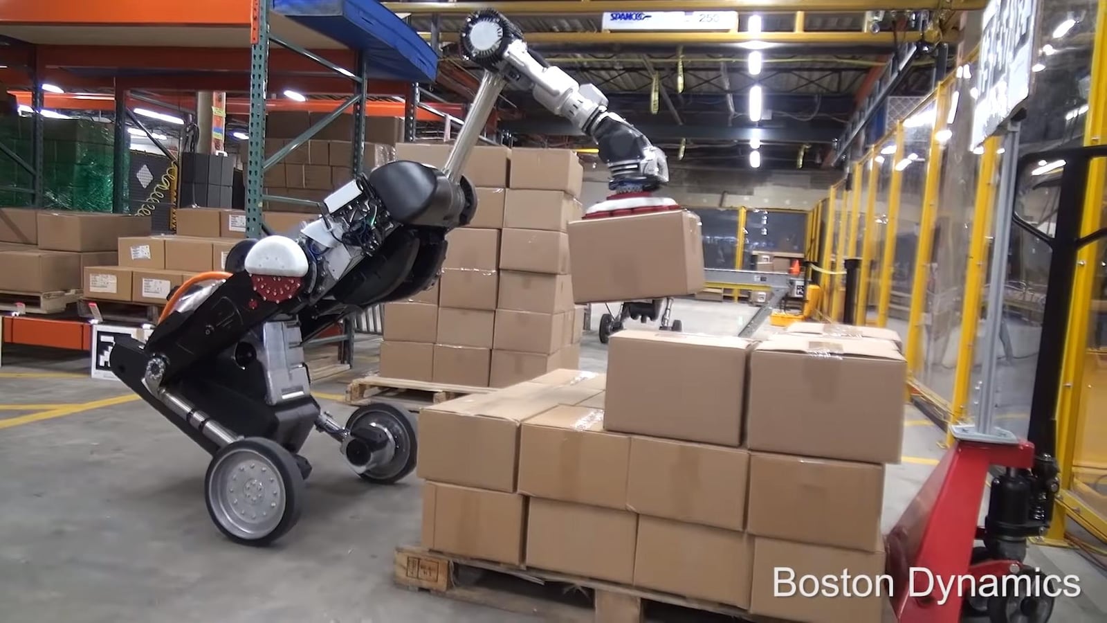 Une photo du robot Handle tenant une boîte au bout de son bras articulé dans un entrepôt.