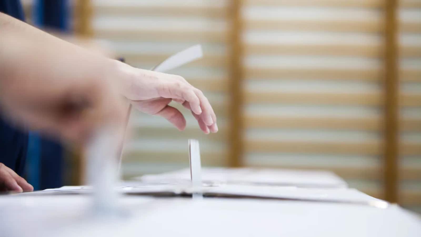 Une main dépose son bulletin de vote dans une boîte de scrutin. 