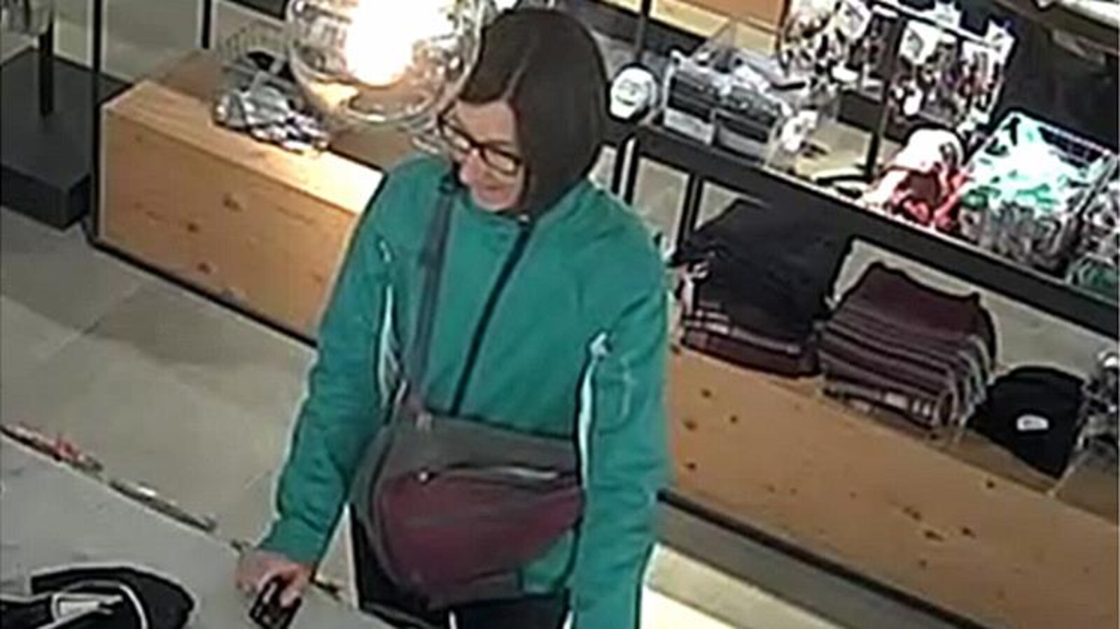 Image tirée d'une caméra de surveillance démontrant une femme devant un comptoir de magasin, prête à payer.