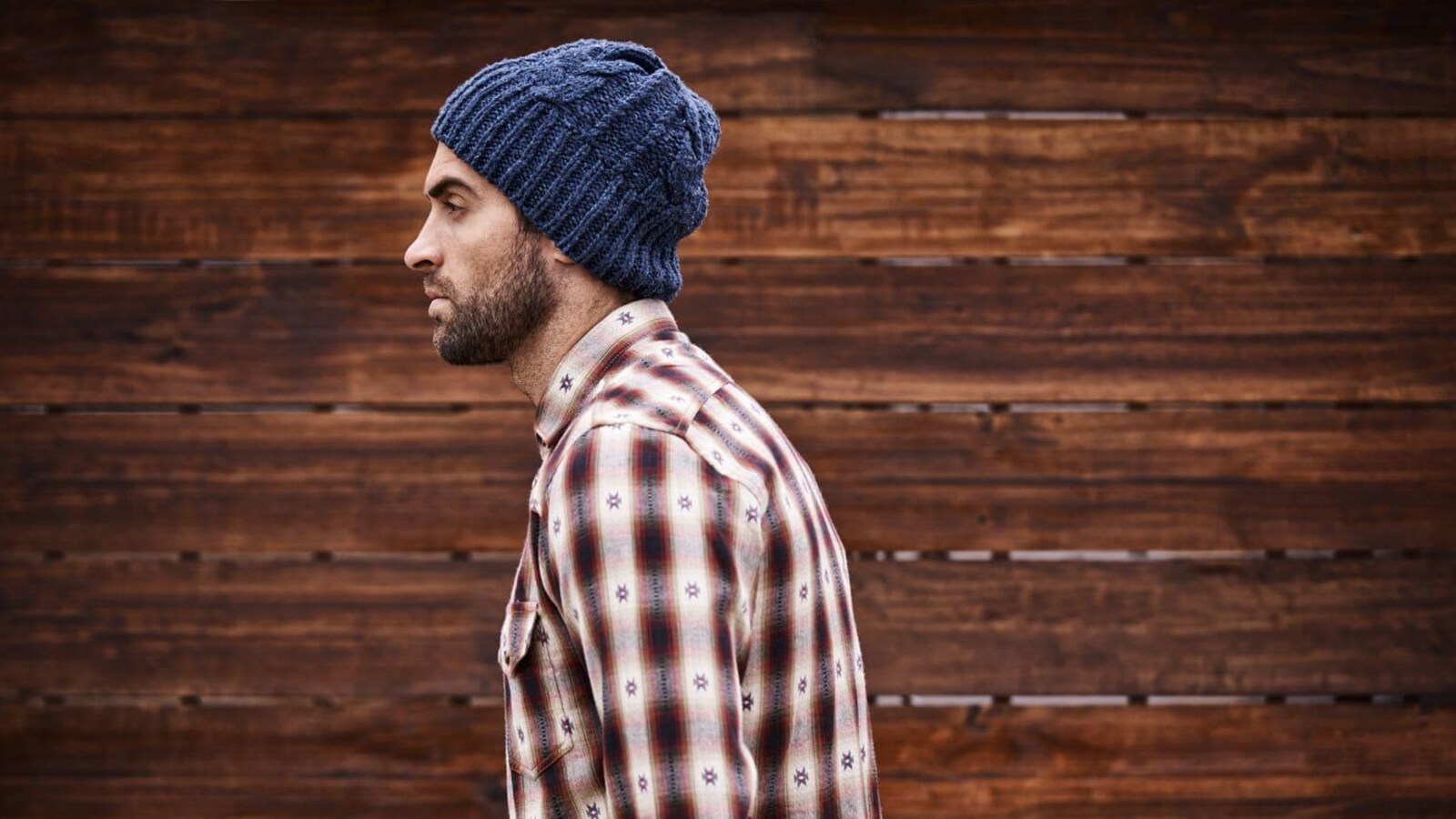 Un homme de profil avec une barbe portant une chemise et une tuque regarde devant lui.