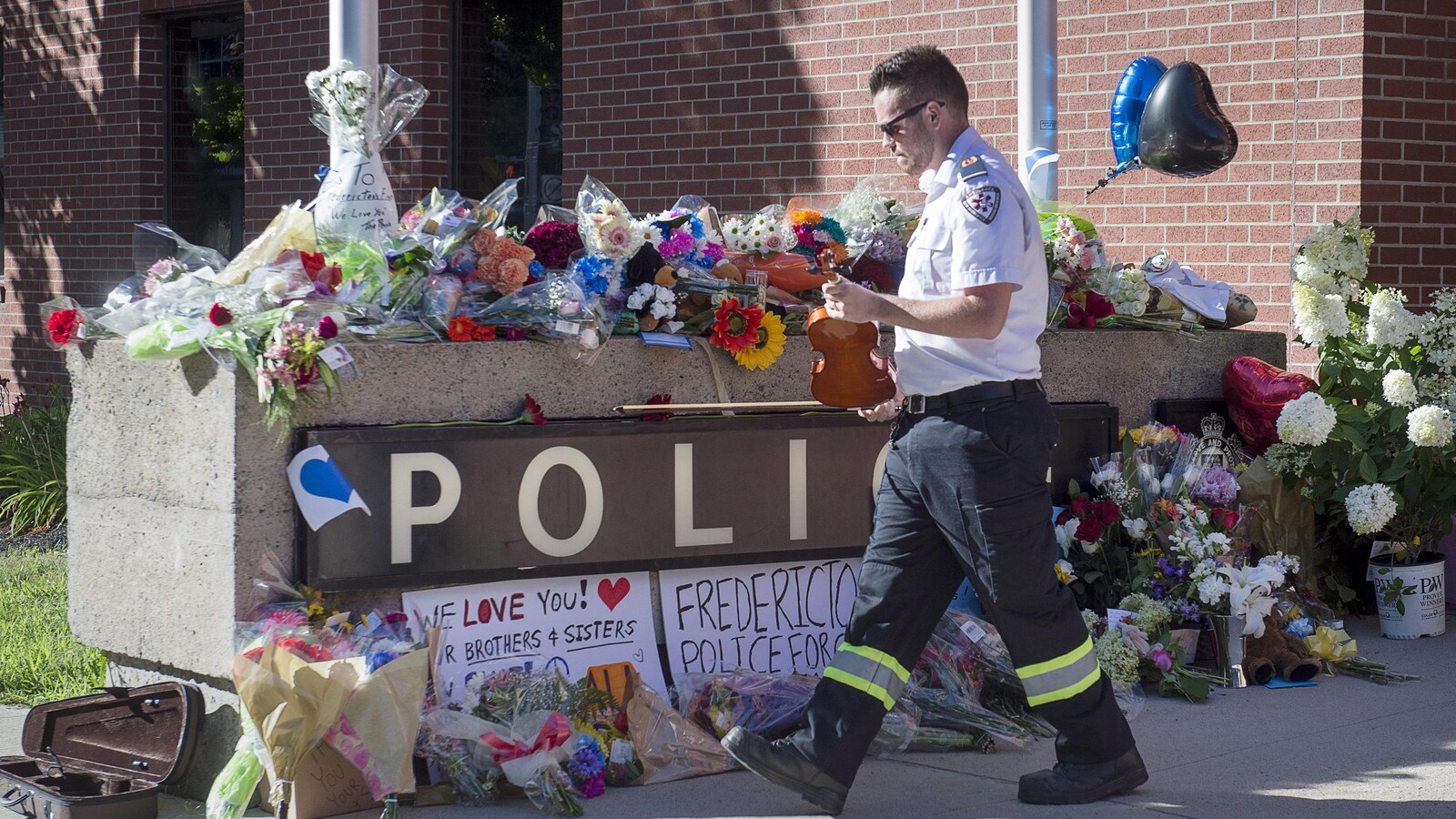 Un paramédic dépose le violon avec lequel il a joué un air en hommage aux policiers morts en service à Fredericton, dans un endroit où de nombreuses gerbes de fleurs ont été placées.