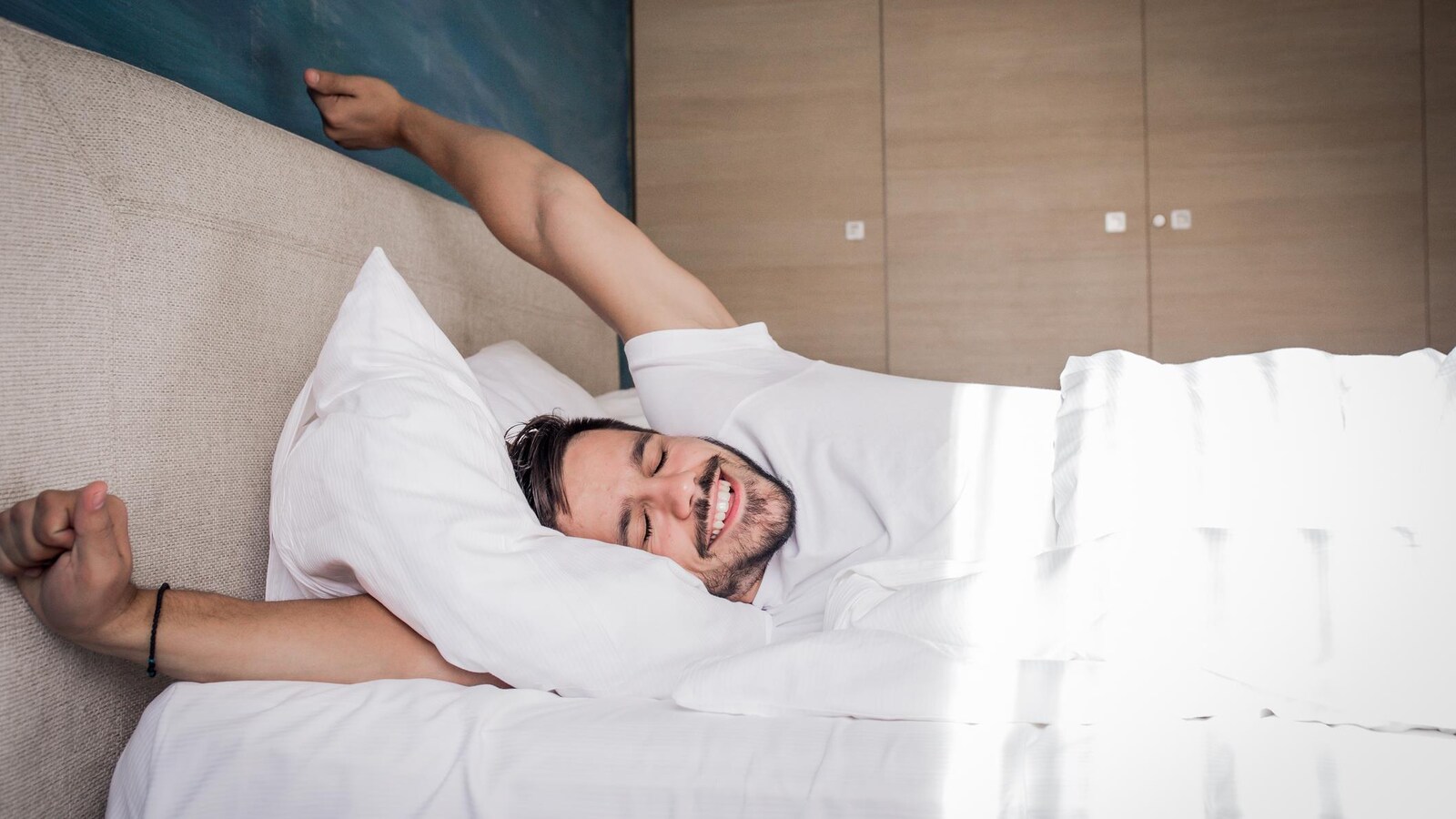 Un homme s'étire dans un lit.