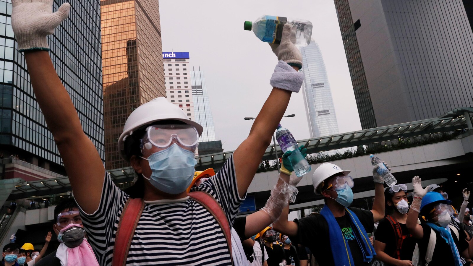 Des manifestants masqués et casqués lèvent les mains en l'air.
