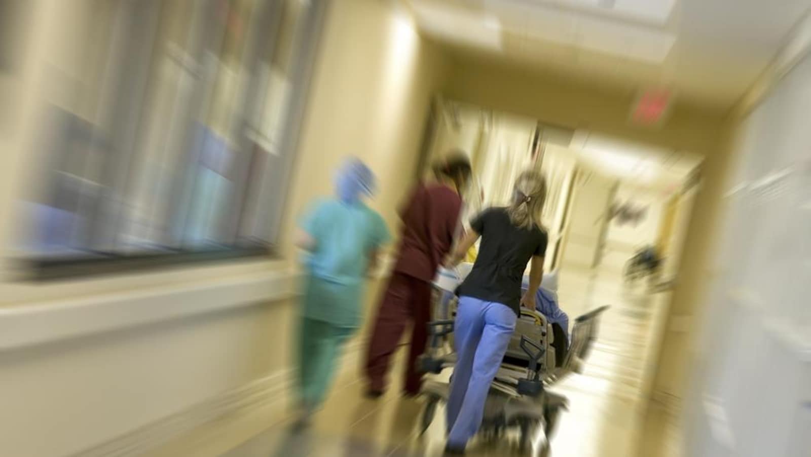 Une infirmière fait rouler un lit dans un couloir d'hôpital.