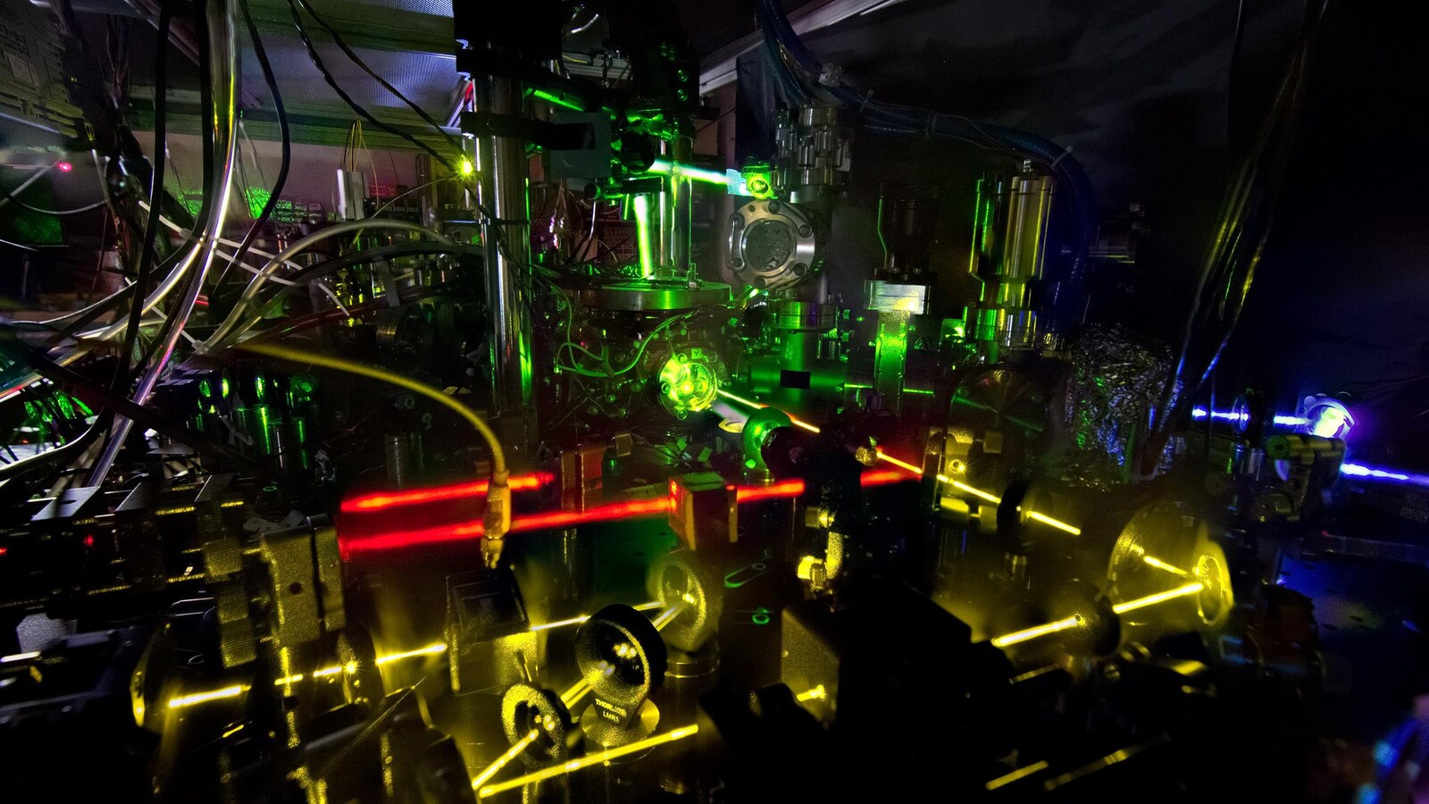 On voit une série de rayons laser rouges, jaunes et verts qui sont reflétés et passent à travers divers instruments.