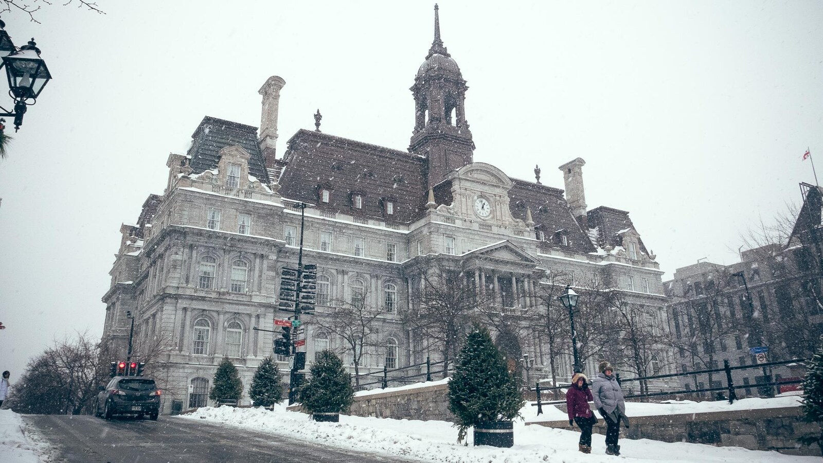 Des gens se baladent sur la place Jacques-Cartier devant l'hôtel de ville de Montréal, alors qu'une fine neige tombe dans le Vieux-Montréal.