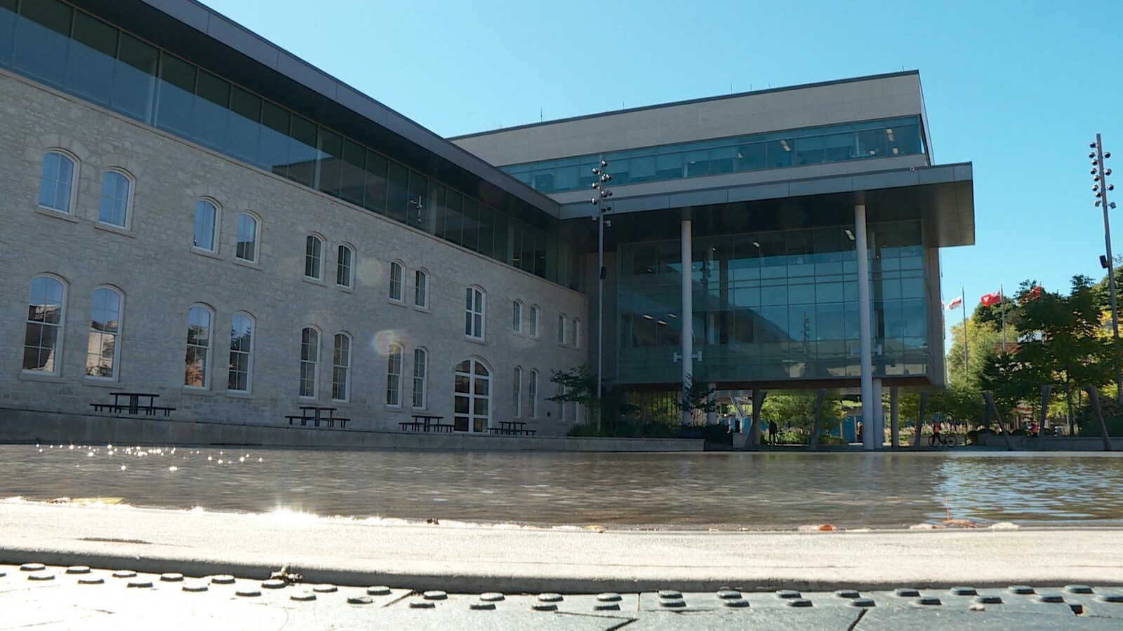 Grand bâtiment avec beaucoup de fenêtres vu en contre-plongée. On voit une étendue d'eau en face de l'édifice.
