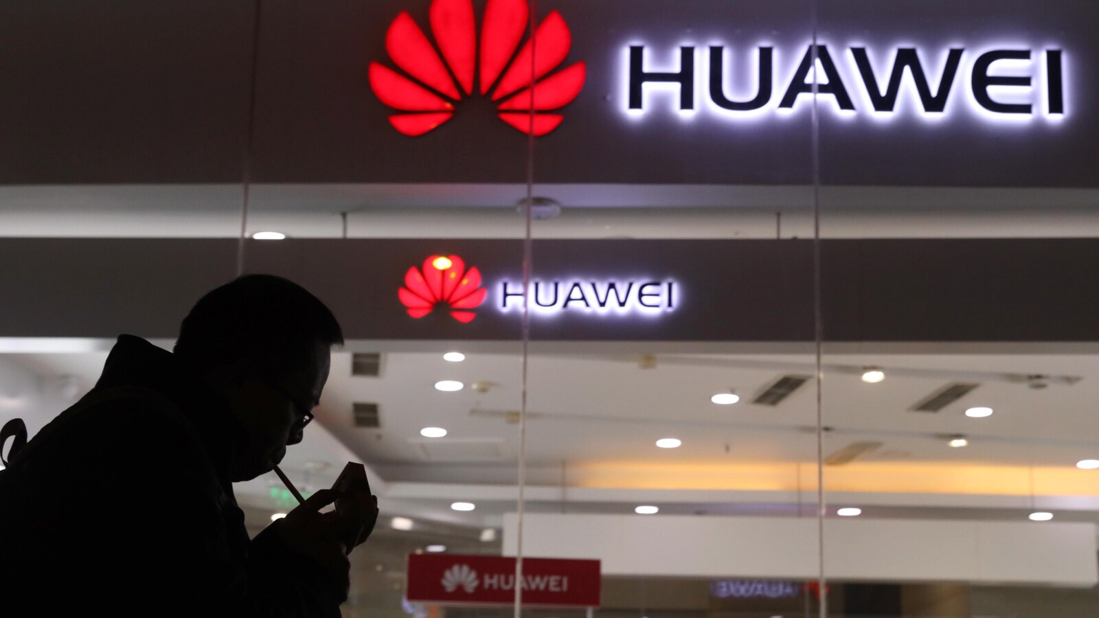 Un homme fume une cigarette devant l'entrée d'un magasin Huawei.