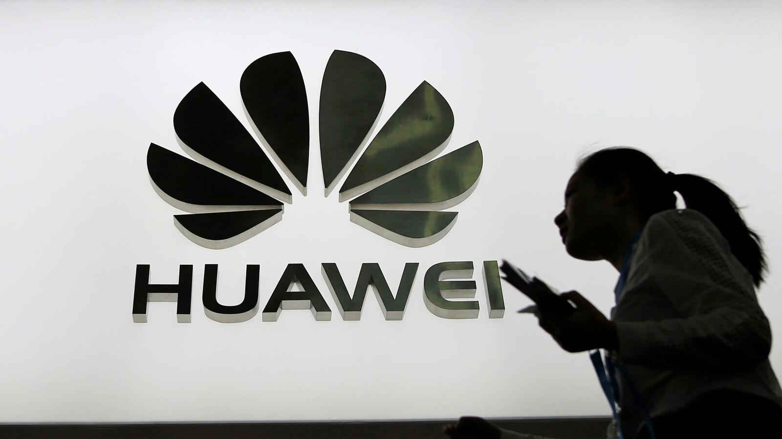 Des personnes marchent devant un panneau lumineux montrant le logo de Huawei.
