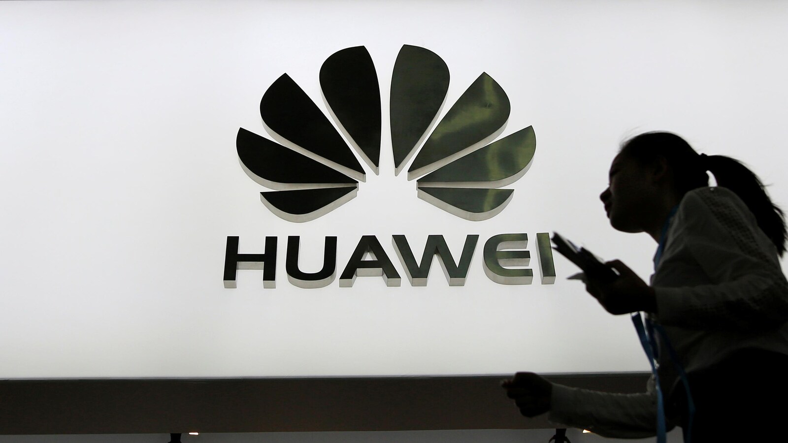Des personnes marchent devant un panneau lumineux montrant le logo de Huawei.