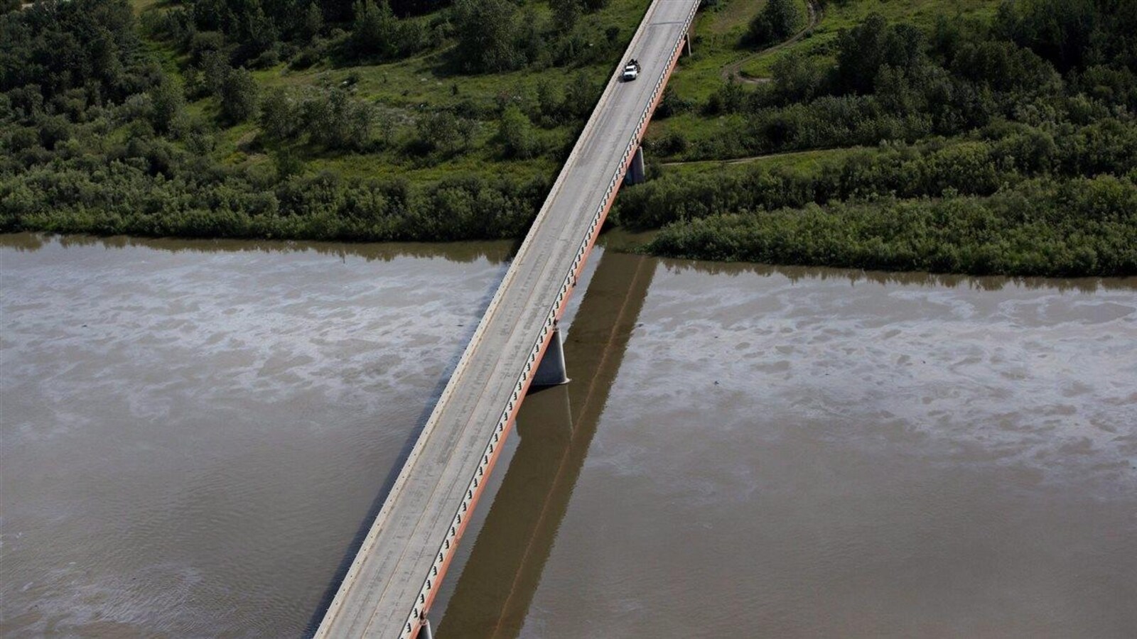 Vue aérienne de la nappe de pétrole sur la rivière Saskatchewan Nord. La rivière coule sous un pont qui mène à une rive boisée.
