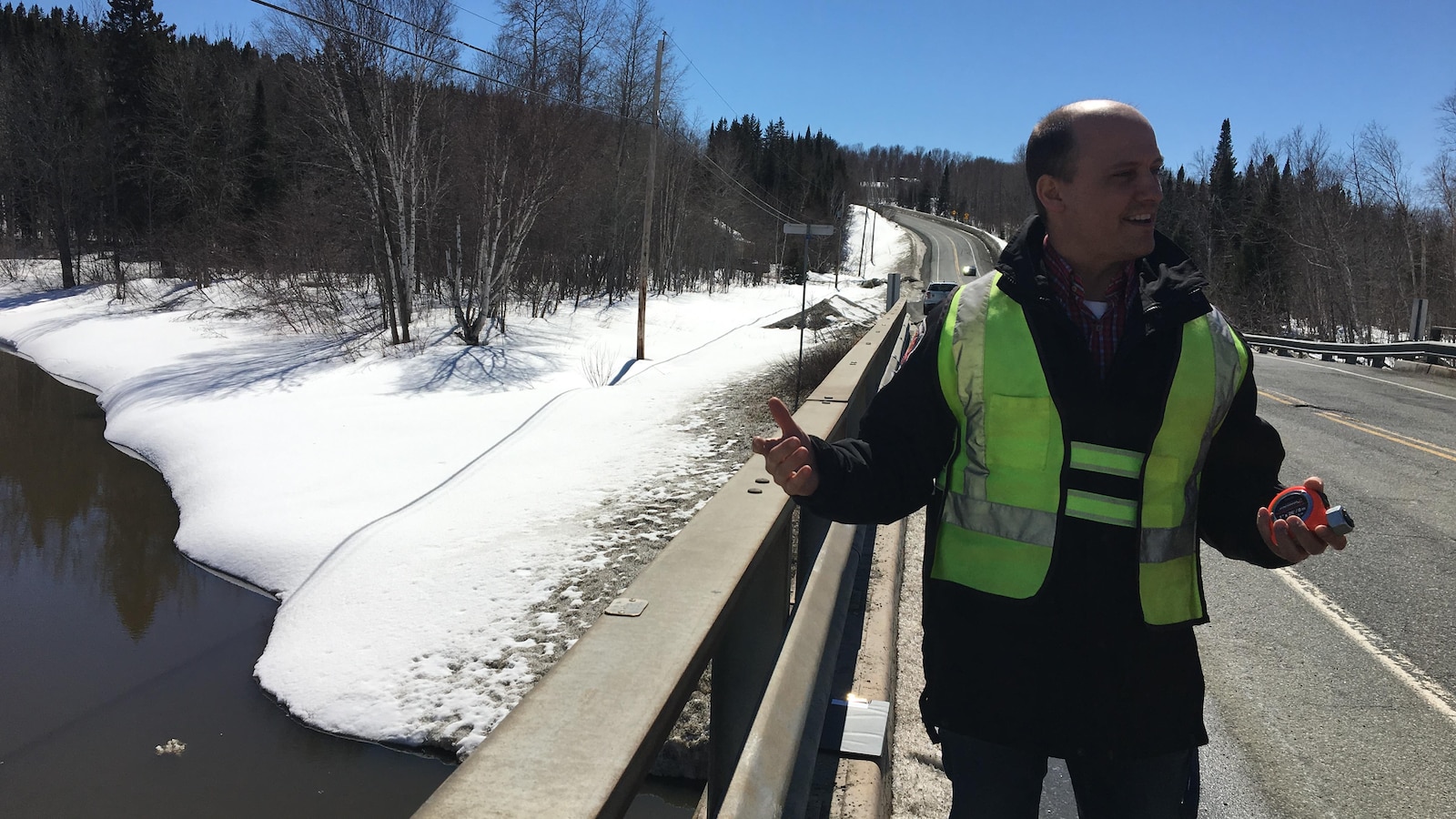 Un homme tient un ruban à mesurer sur un pont, s'apprêtant à mesurer le niveau de l'eau.