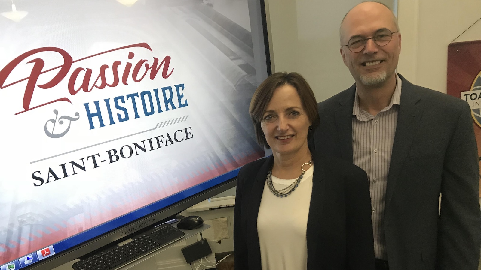 Un homme et une femme sont debout à côté d'un écran où l'on peut lire « Passion et histoire Saint-Boniface».