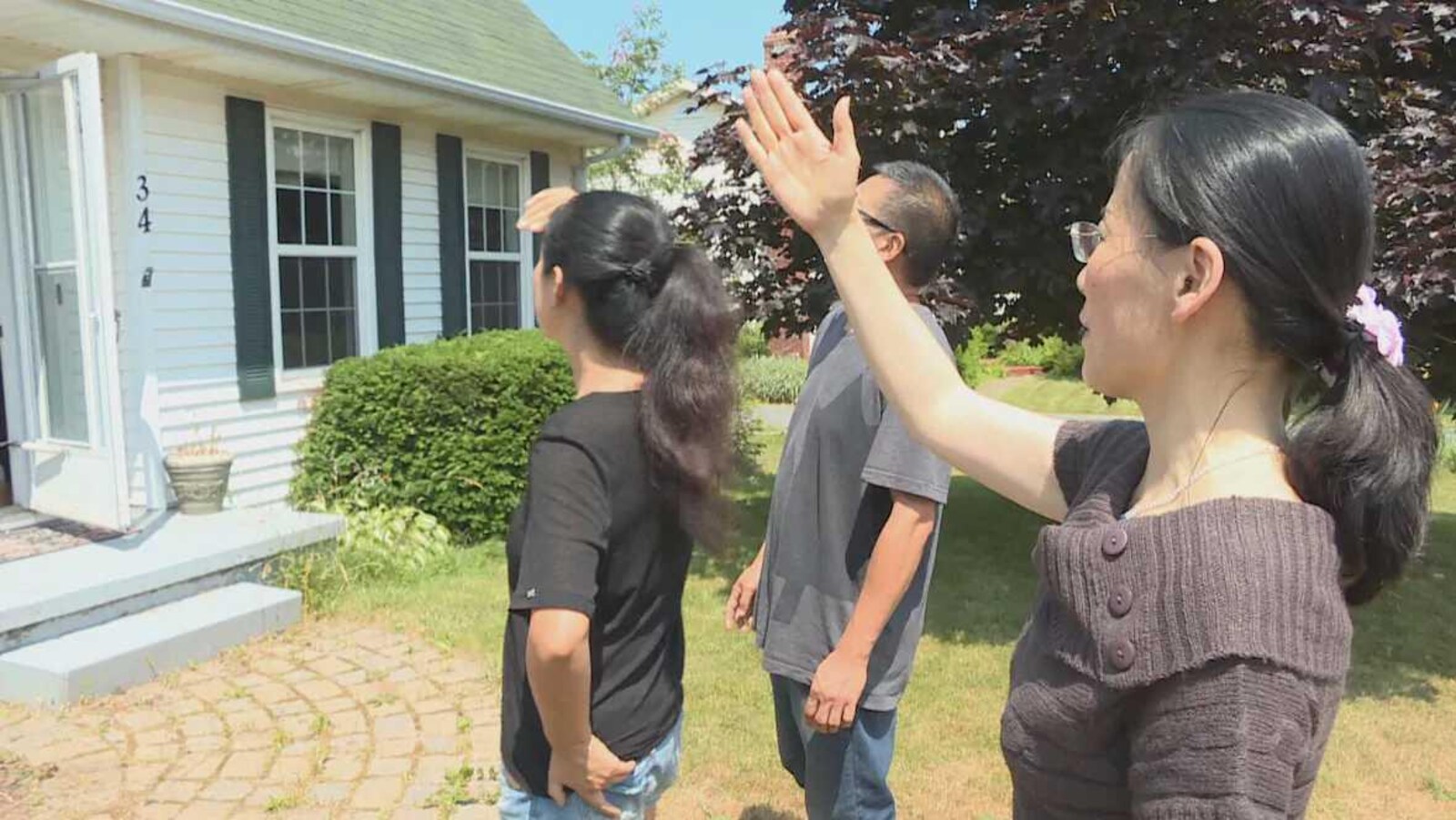Une agente immobilière et deux acheteurs devant une maison.