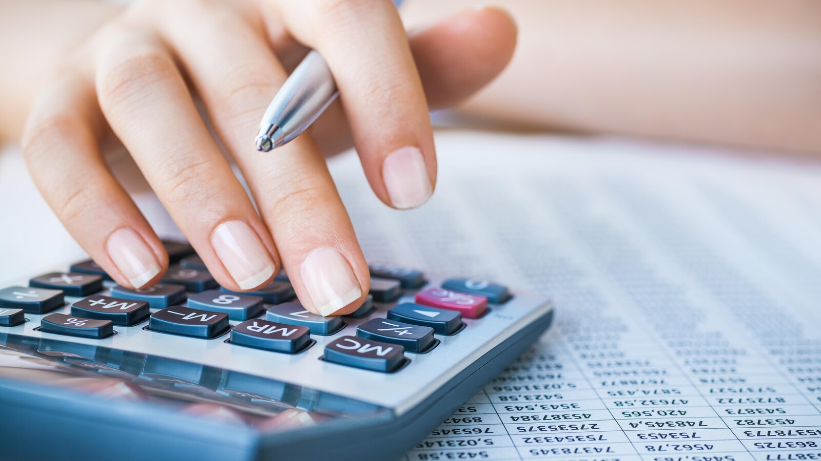 Une personne tenant un stylo dans sa main semble taper des numéros sur calculatrice.