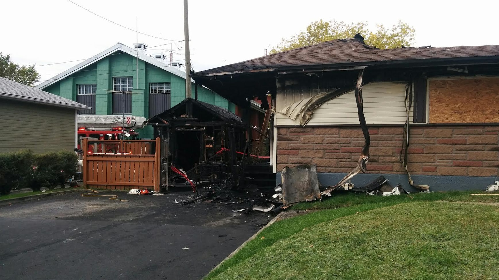 Photographie d’une maison unifamiliale endommagée par les flammes. Le toit de la demeure s’est en partie effondré. Un cabanon situé sur le côté de la maison est complètement calciné.