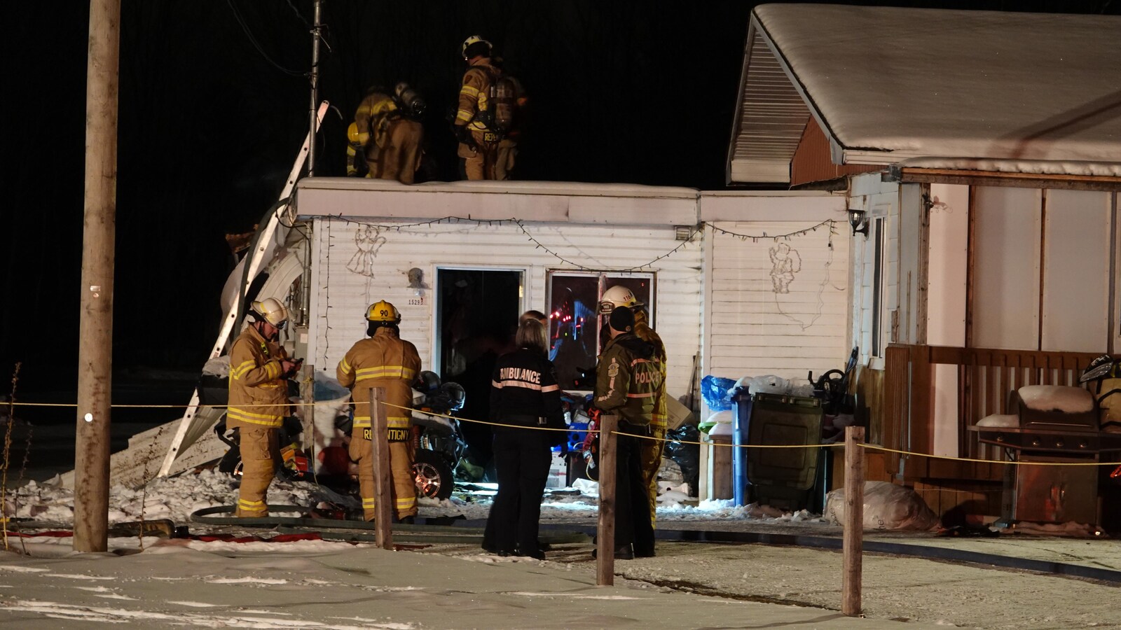 Cinq pompiers, une ambulancière et un policier s'affaire dans le bungalow adjascent une maison.
