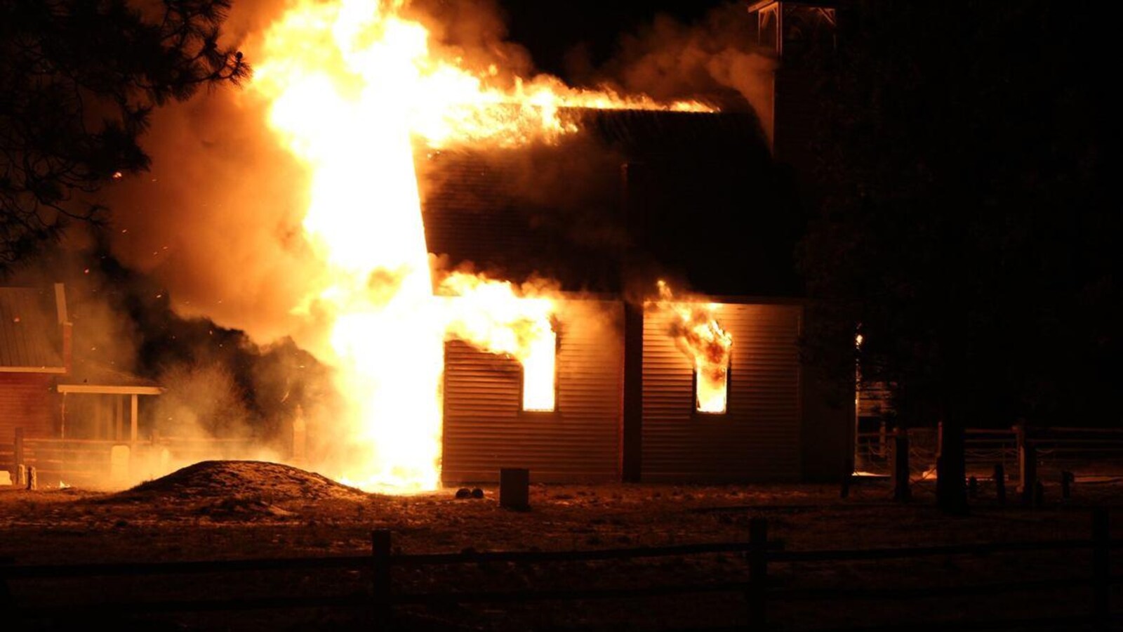 Des flammes de la hauteur du clocher sortent par la porte et les fenêtres de l'église, projetant un nuage de fumée et des étincelles.