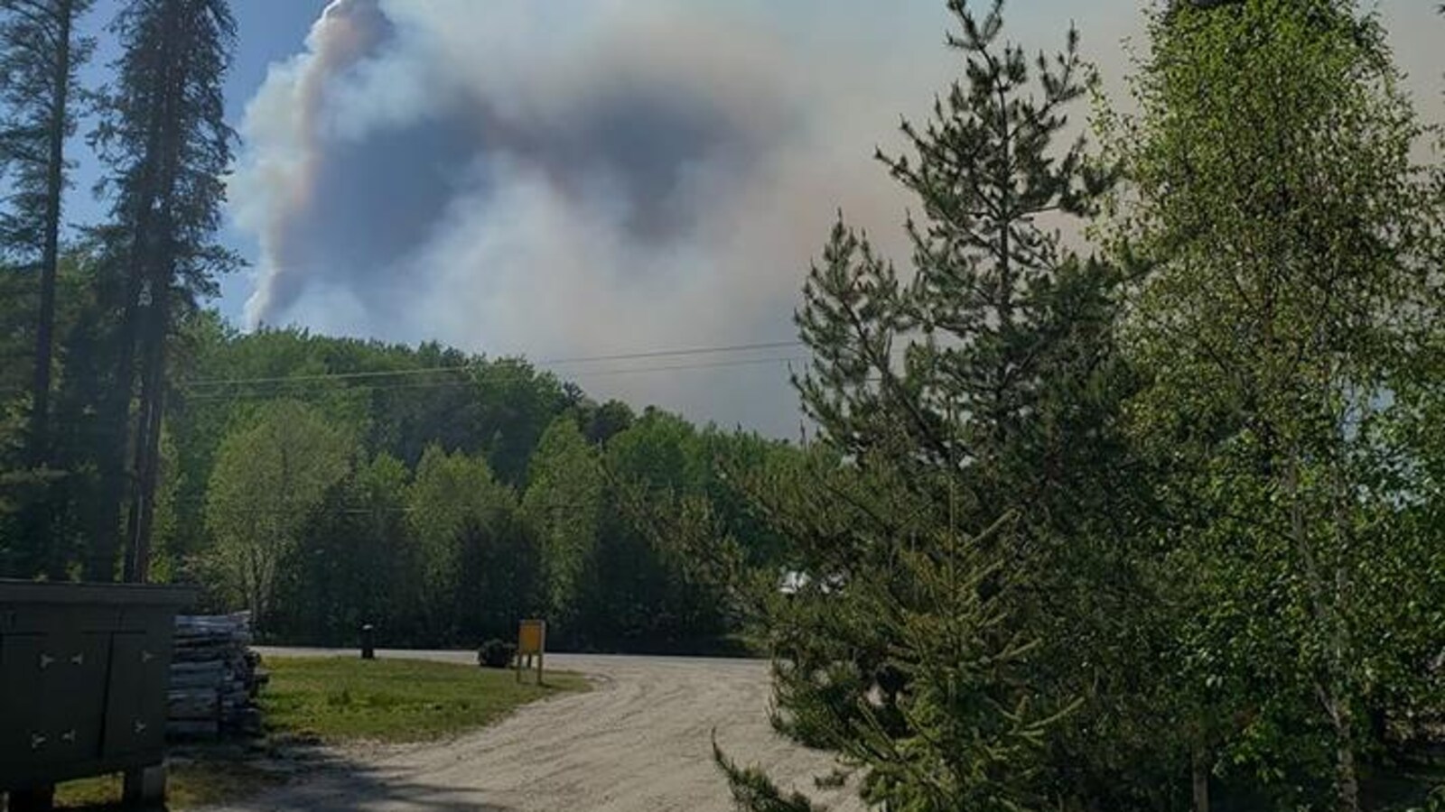 Des arbres et de la fumée au loin près d’une route rurale.
