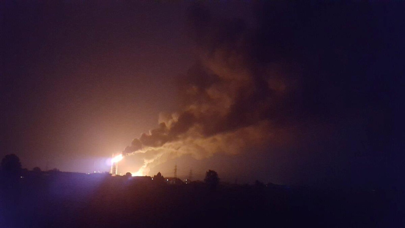 Un grand incendie et des colonnes de fumée au loin dans la nuit.