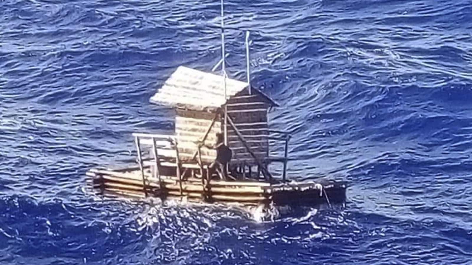 Un individu sur un radeau de bois en pleine mer.