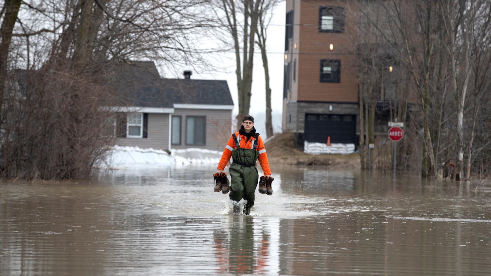 Un homme marche dans l'eau avec des bottes dans ses mains.