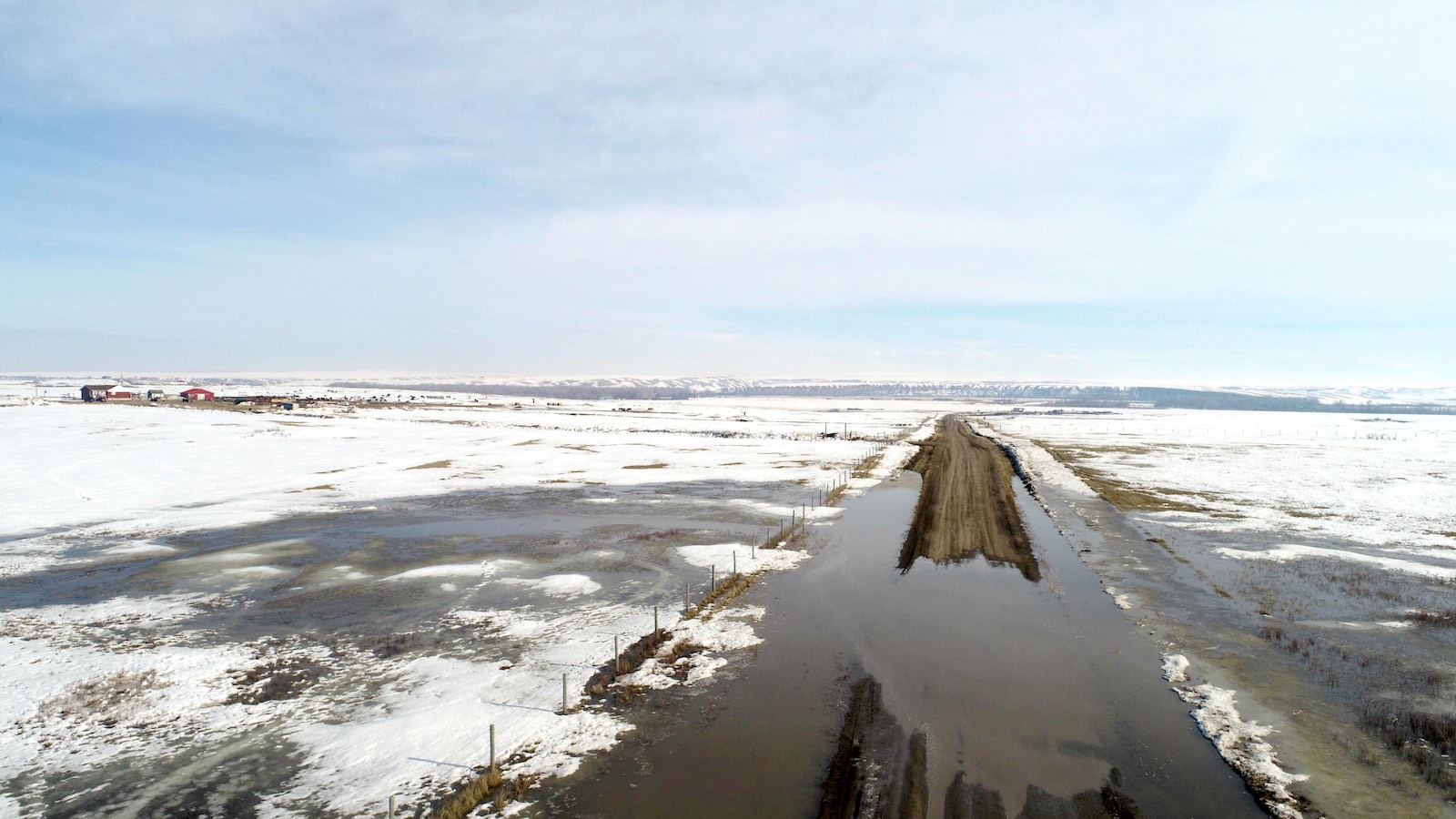 Une route recouverte d'eau au milieu de champs couverts de neige.