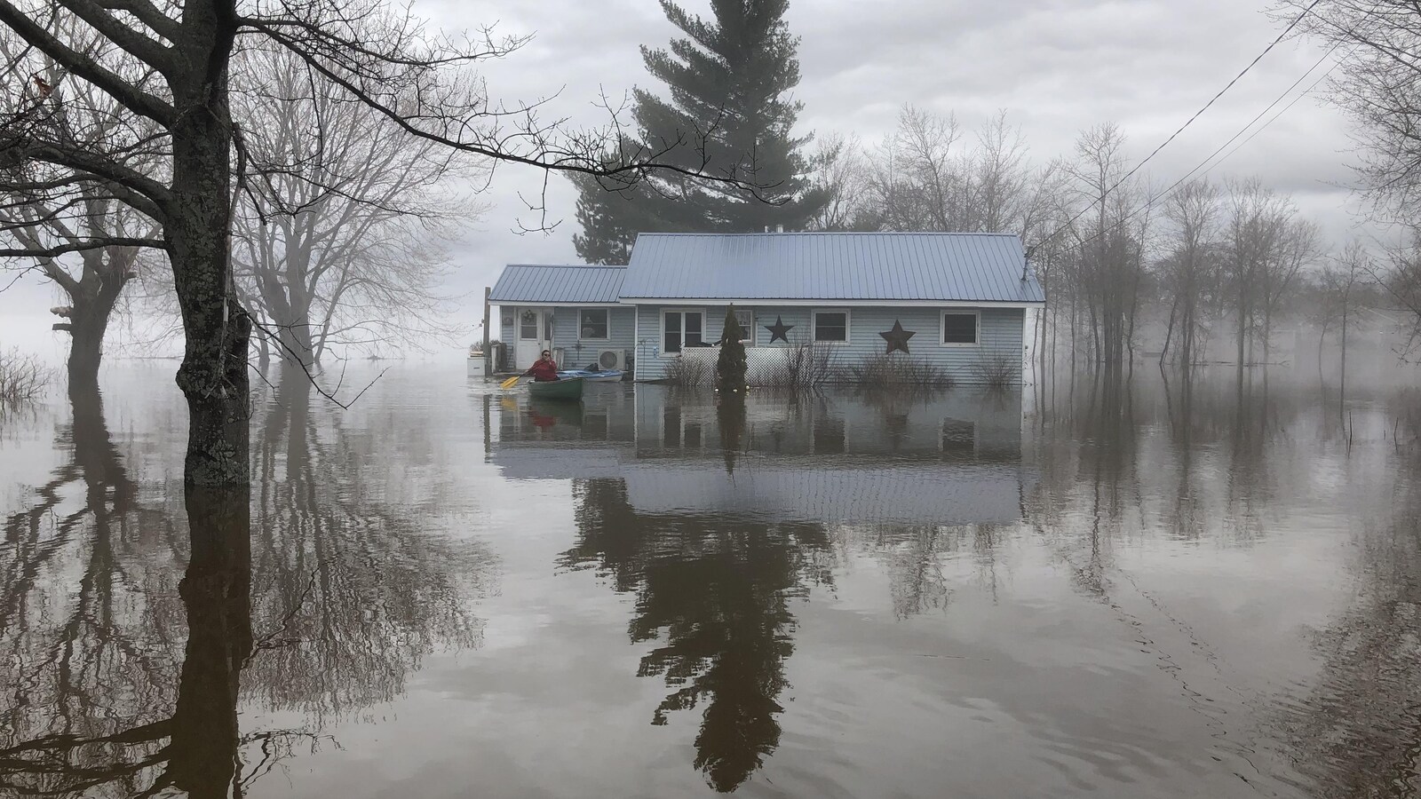 Une femme en canot devant une maison inondée