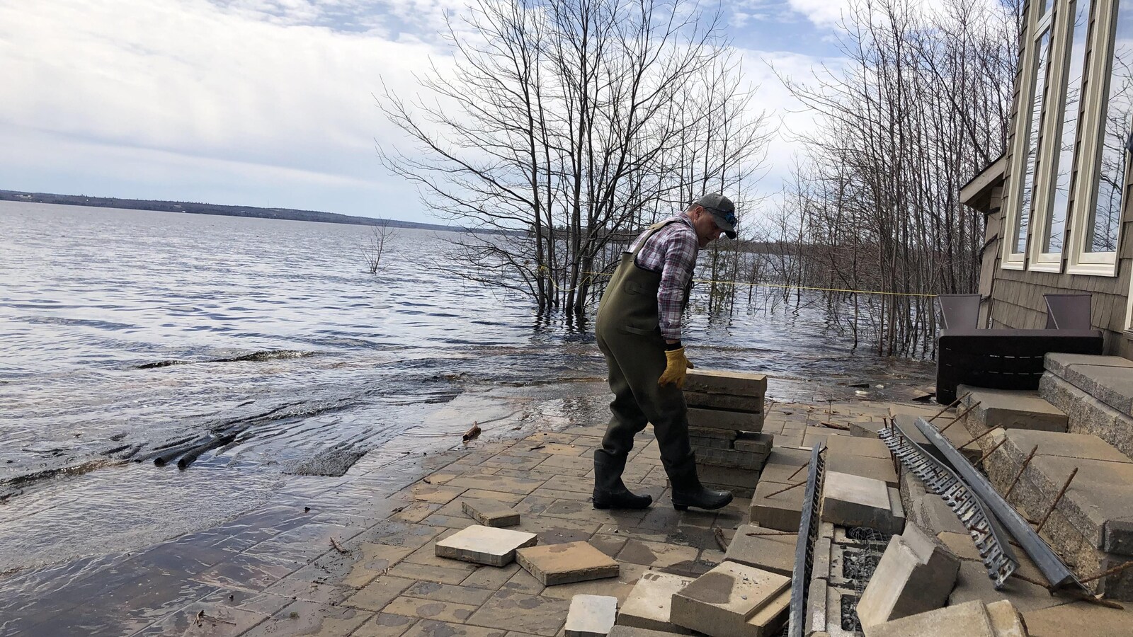 Un homme en bottes de caoutchouc vérifie les dommages à sa propriété, à Grand Lake.