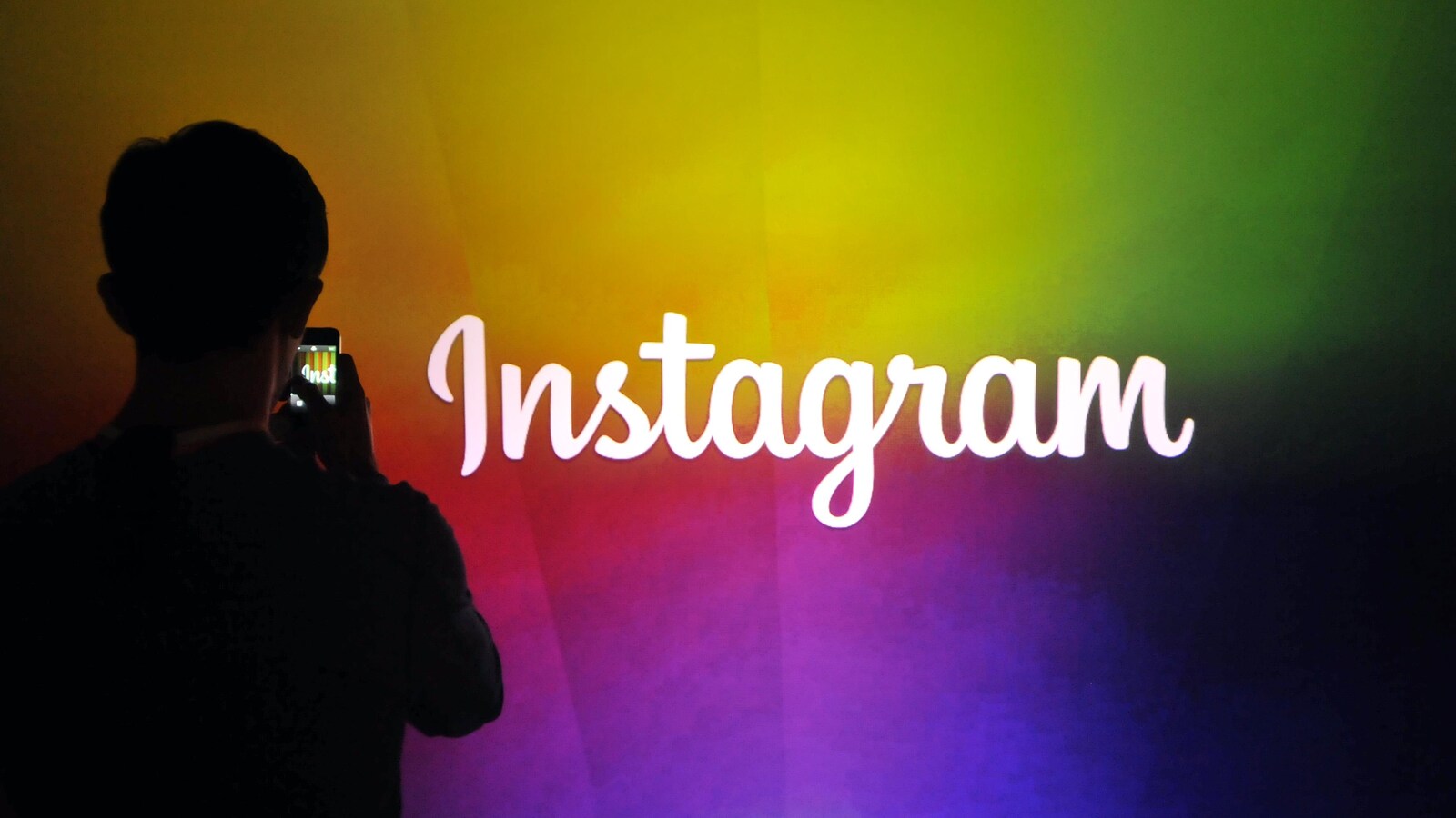 Un homme prend en photo le logo d'Instagram écrit en blanc sur un mur multicolore.
