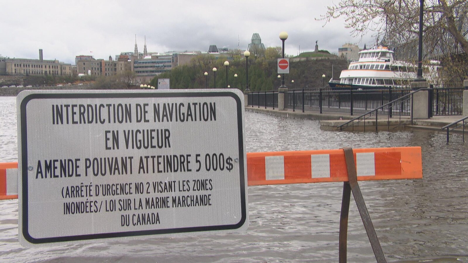 Une barrière d'interdiction aux abords de la rivière des Outaouais devant un bateau de croisière.