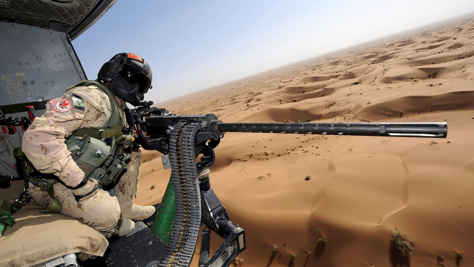 Un mitrailleur installé dans un hélicoptère survolant un désert.