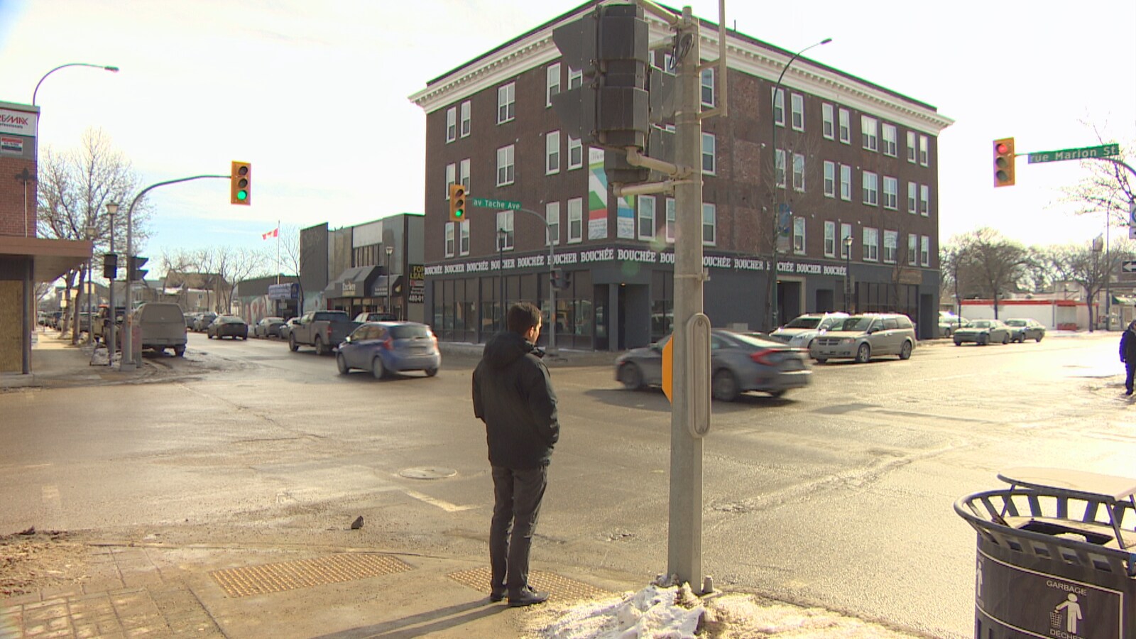 Un homme attend de traverser la rue à une intersection où passent plusieurs voitures.