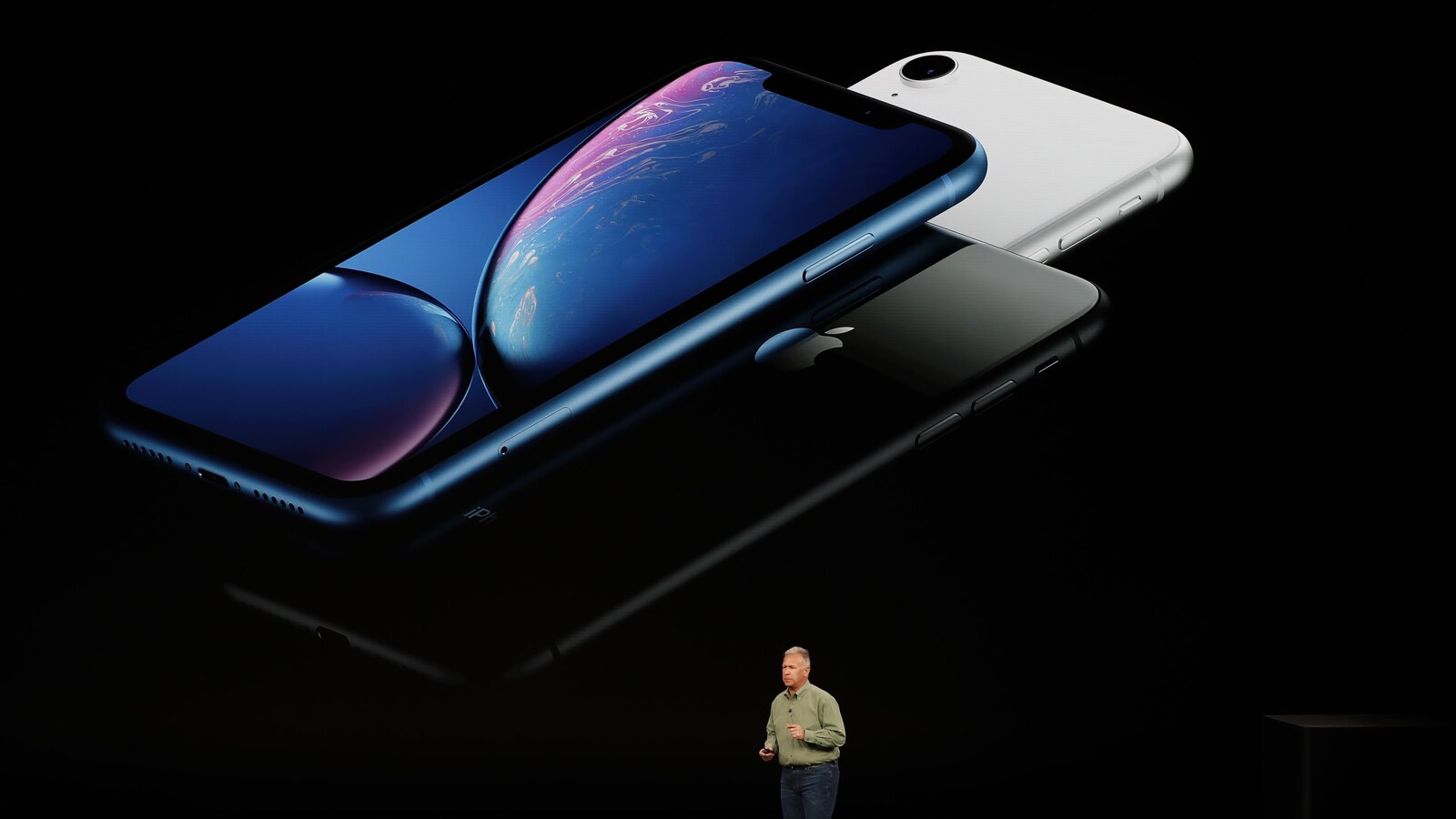 Une photo montrant trois iPhone X R sur un écran géant. Un homme est debout devant l'écran.
