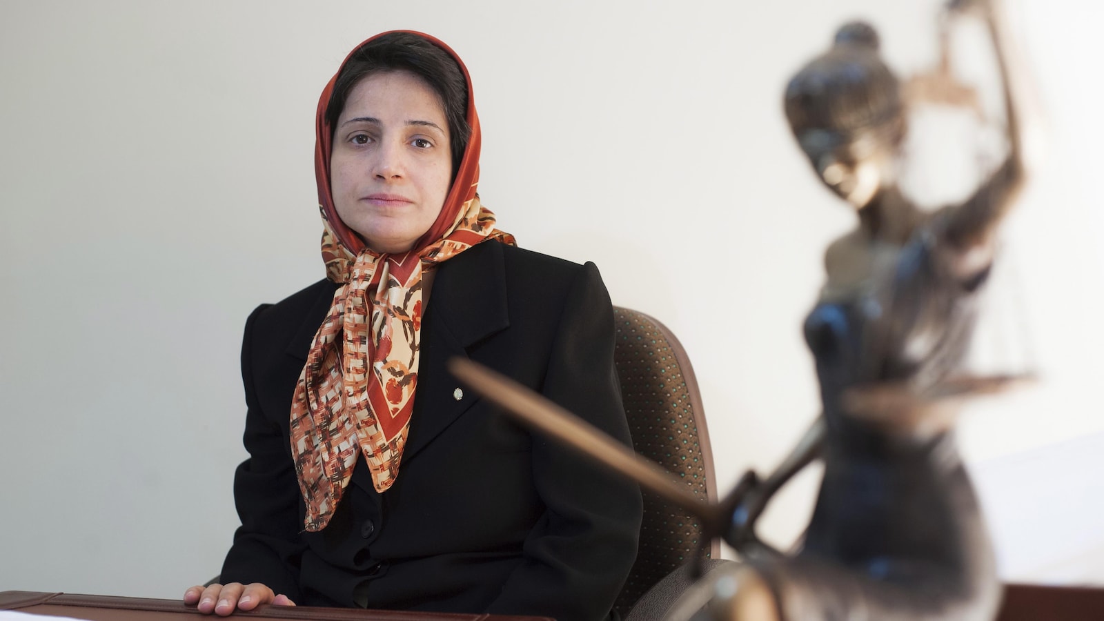 Nasrin Sotoudeh, assise à une table, regarde l'objectif alors qu'on voit une statue de la justice à l'avant-plan.