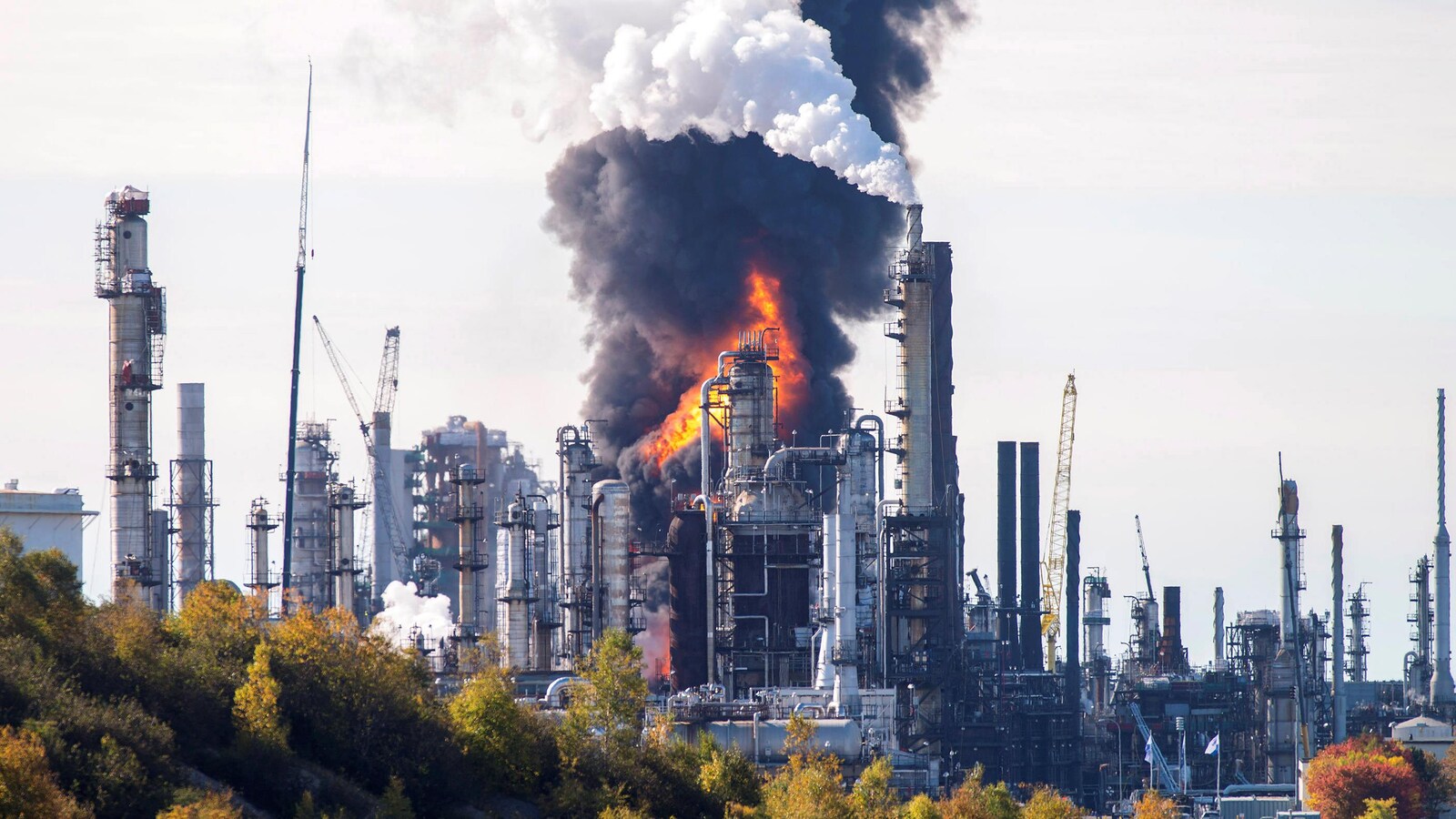 Un incendie est vu au loin, derrière des bâtiments et une colonne de fumée noire s'élève dans le ciel.