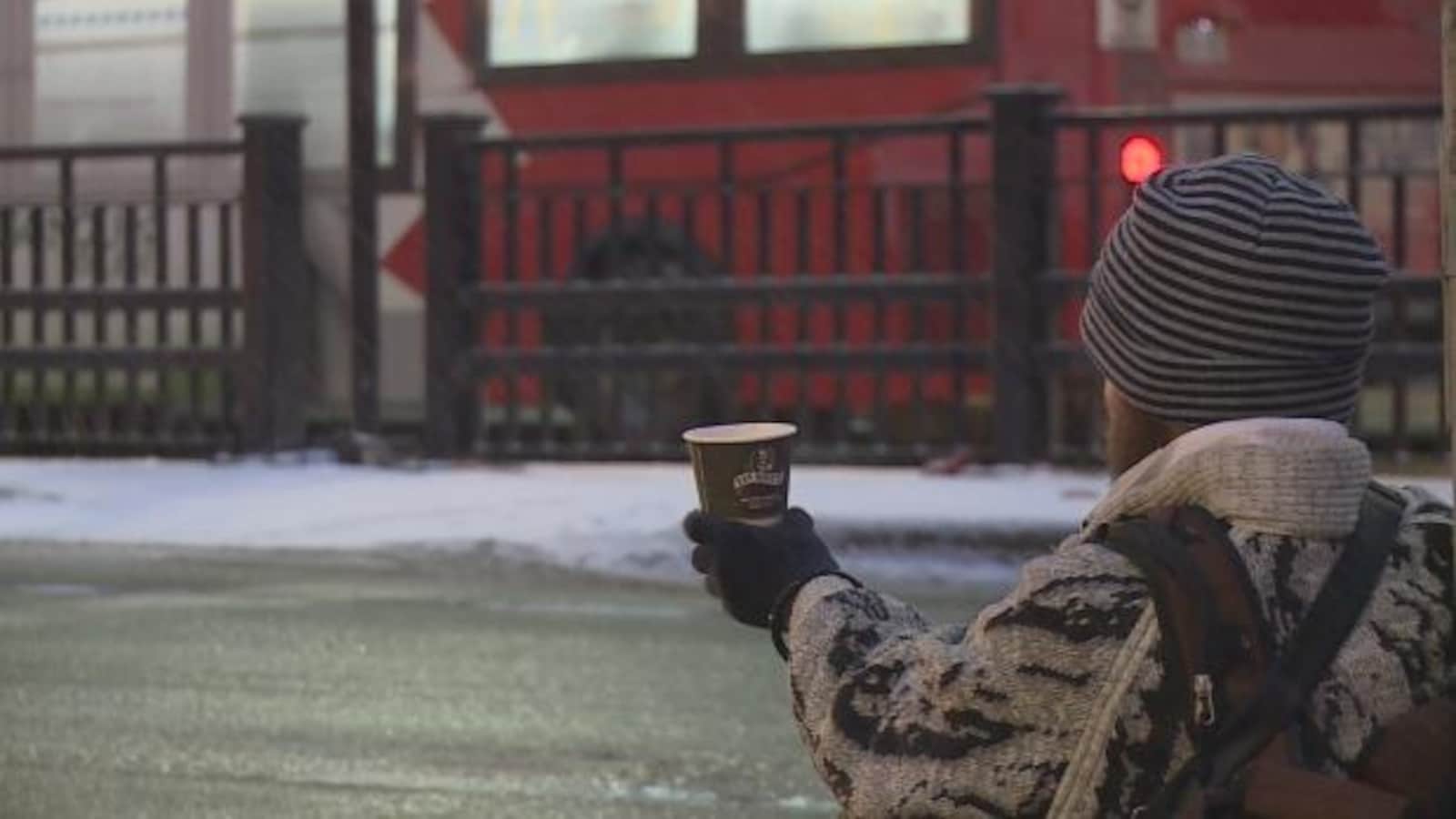 Un homme vu de dos dans la rue qui tend un verre pour recevoir de l'argent.