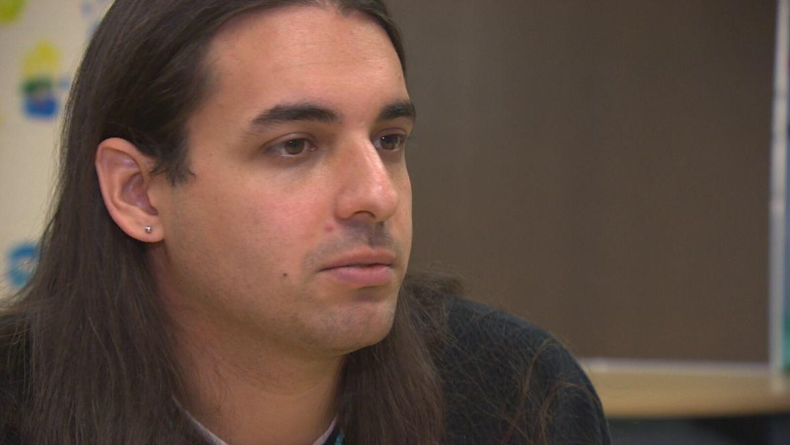 Un jeune homme autochtone aux cheveux longs porte une boucle d'oreille à l'oreille droite.