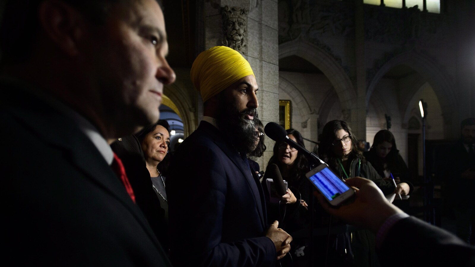 Le chef du Nouveau Parti démocratique (NPD) Jagmeet Singh tient une conférence de presse entouré de journalistes, un micro et un téléphone cellulaire brandis dans sa direction.