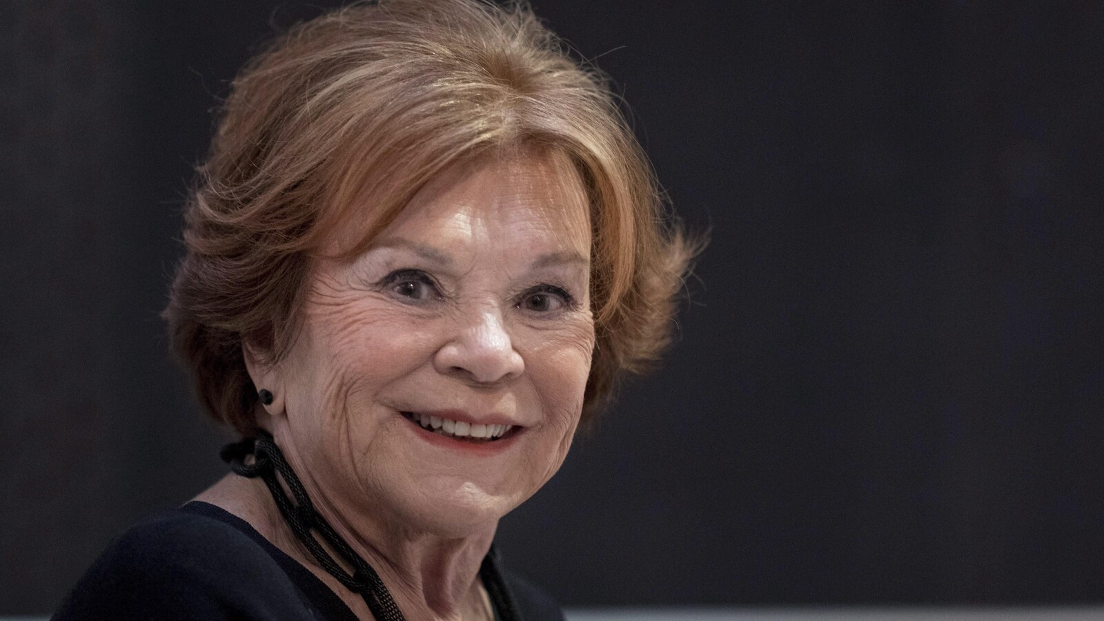 L'auteure, animatrice et intervieweuse Janette Bertrand, devant un fond noir, regarde la caméra en souriant.