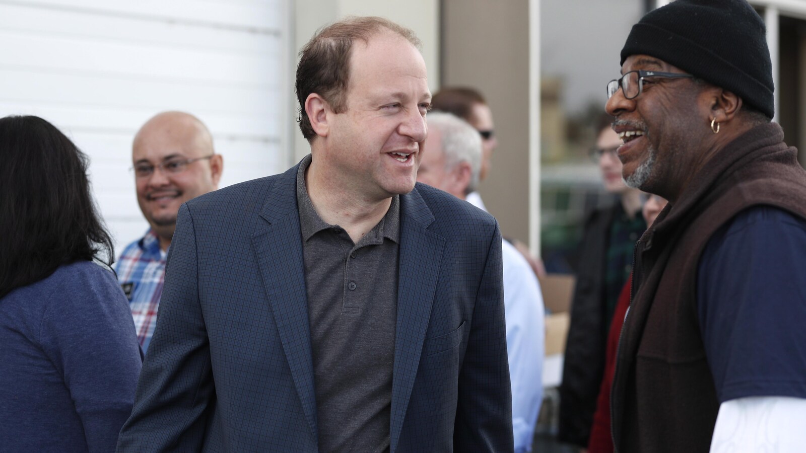 Jared Polis parle à un démarcheur électoral, pendant qu'on voit d'autres personnes derrière.