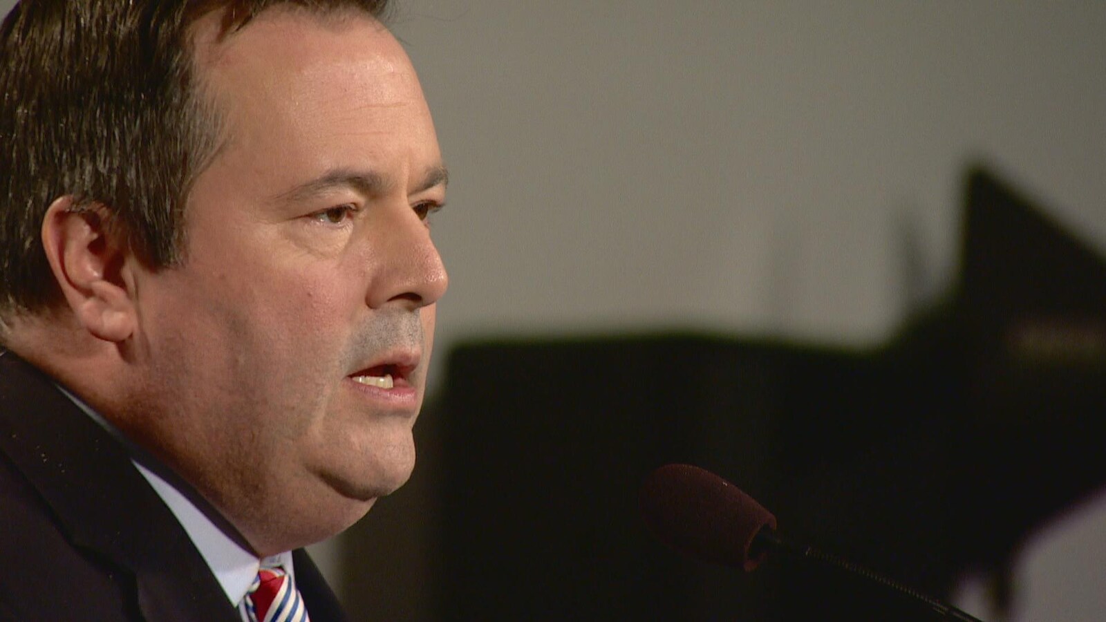 Jason Kenney derrière un micro.