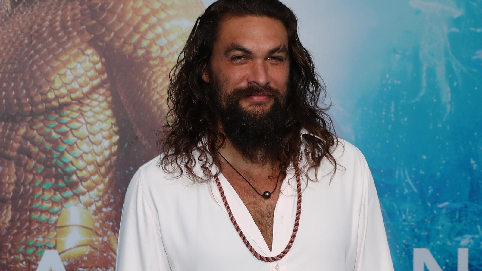 L'acteur souriant devant l'affiche du film Aquaman.