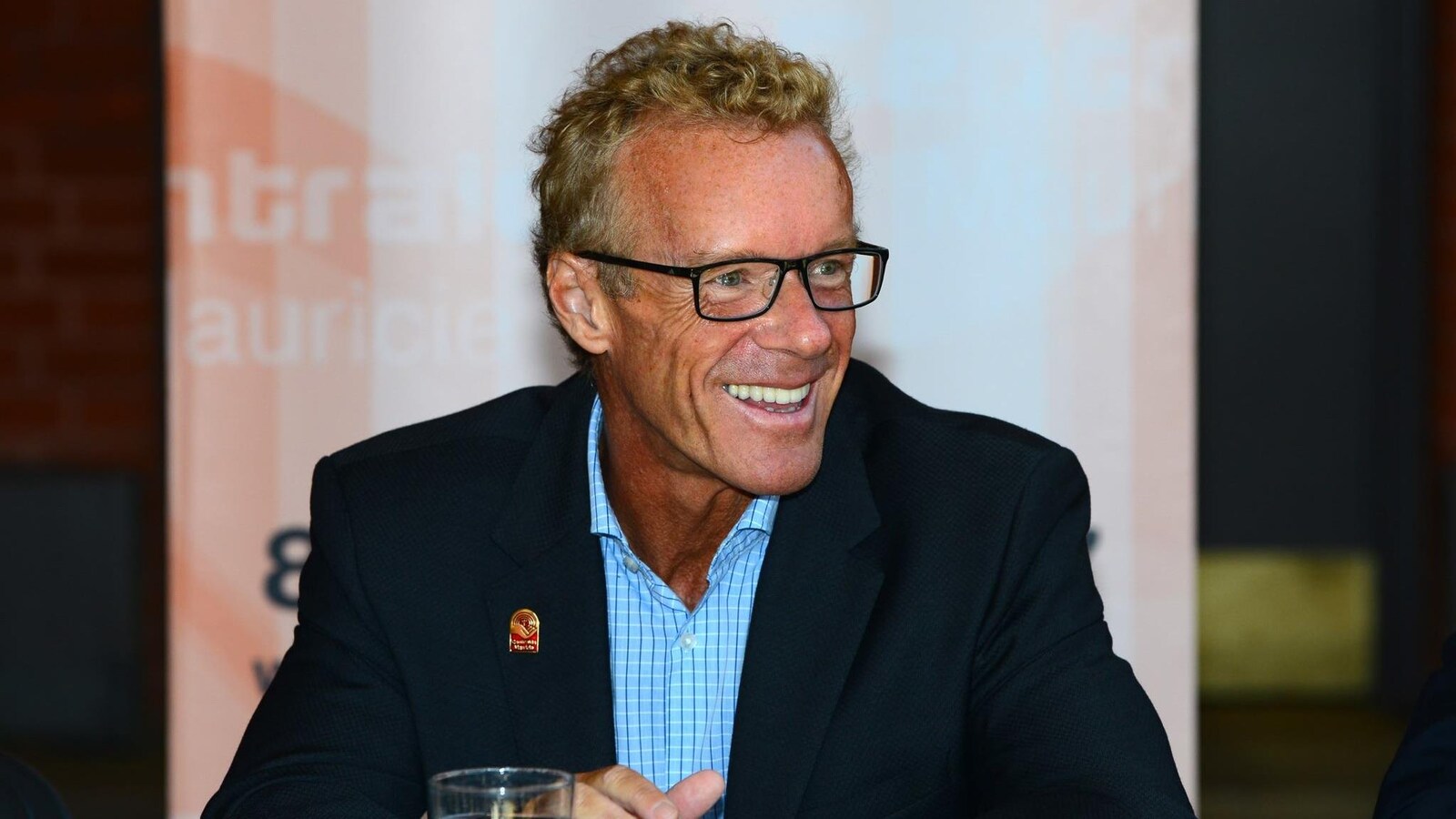 Jean Boulet pose souriant en chemise à carreaux et veston. Il porte des lunettes.